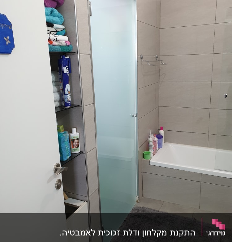 מקלחת עם דלת זכוכית, מגבות ומוצרי טיפוח